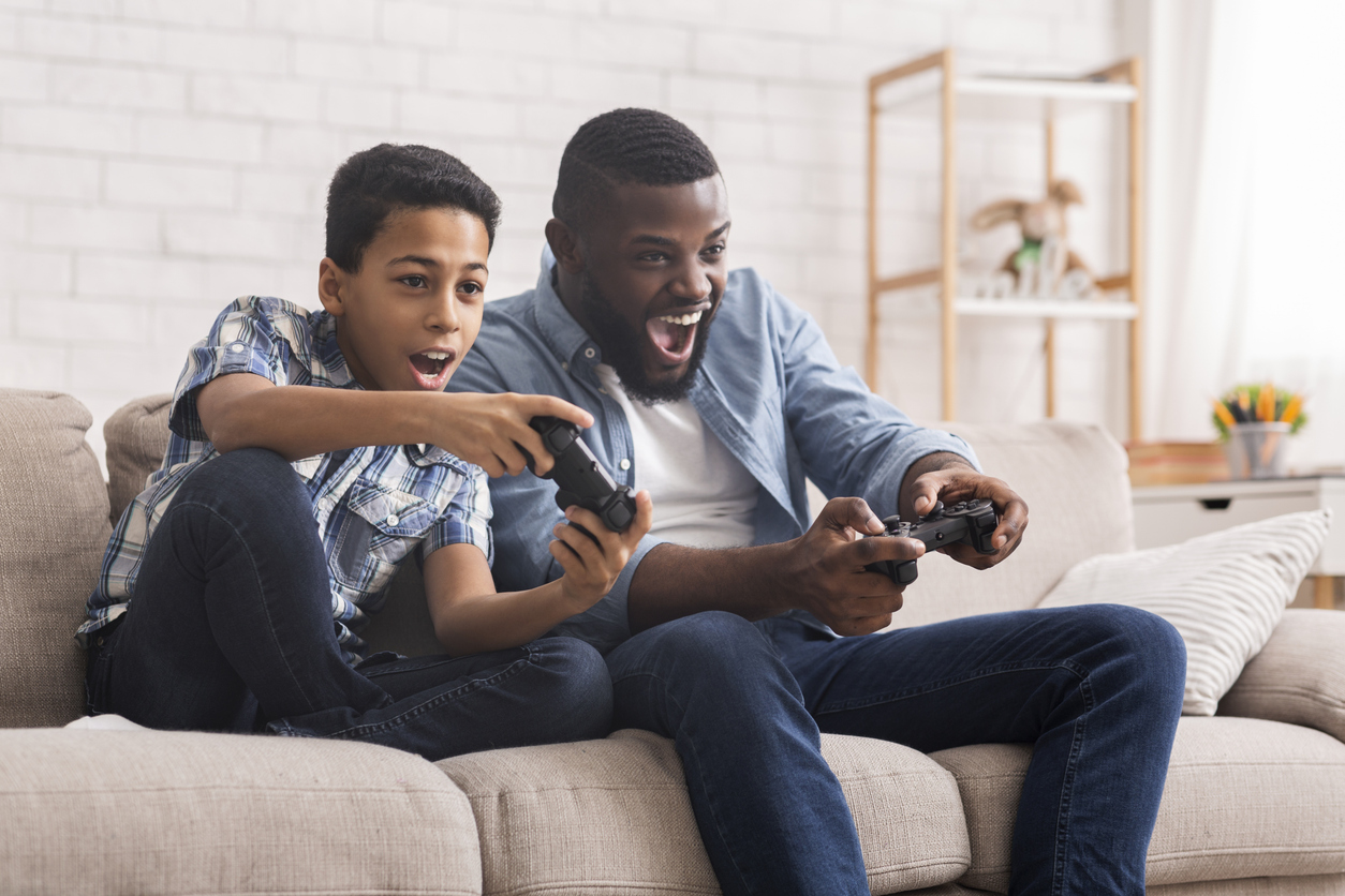 Leisure With Dad. Cheerful Black Father And Son Competing With Each Other In Video Games, Using Joysticks, Having Fun At Home, Free Space