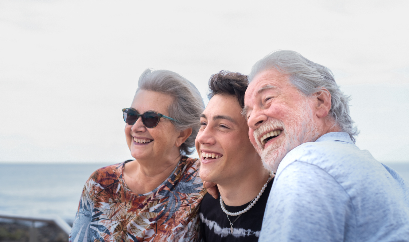 Portrait of three handsome people, smiling happily standing outdoors by the sea. Multi generation family. Grandparents and teenage grandson.