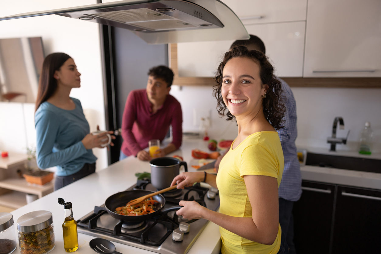 Happy Latin American woman cooking at home with her roommates and looking at the camera smiling