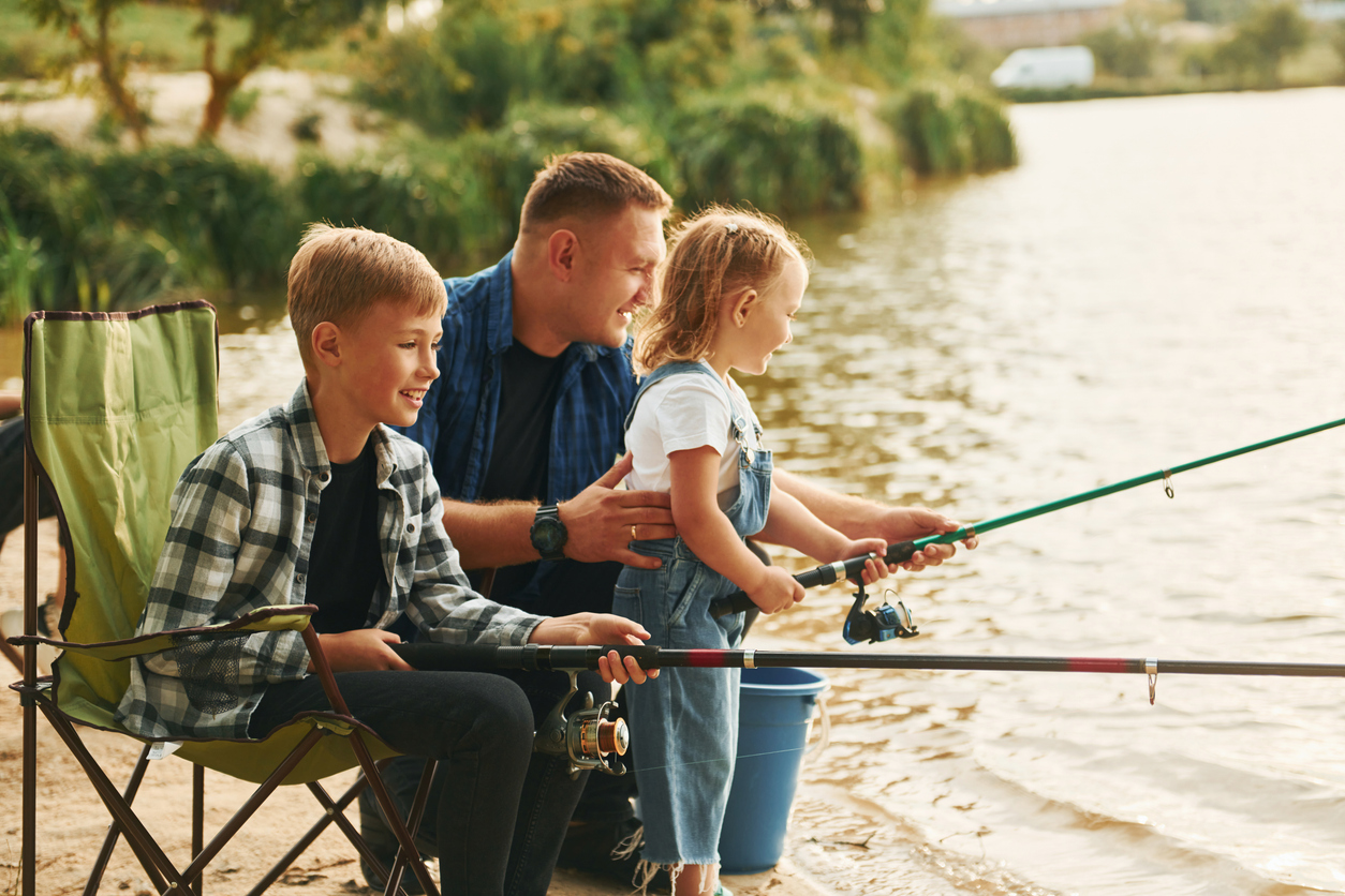 Sitting together. Father with son and daughter on fishing outdoors at summertime.